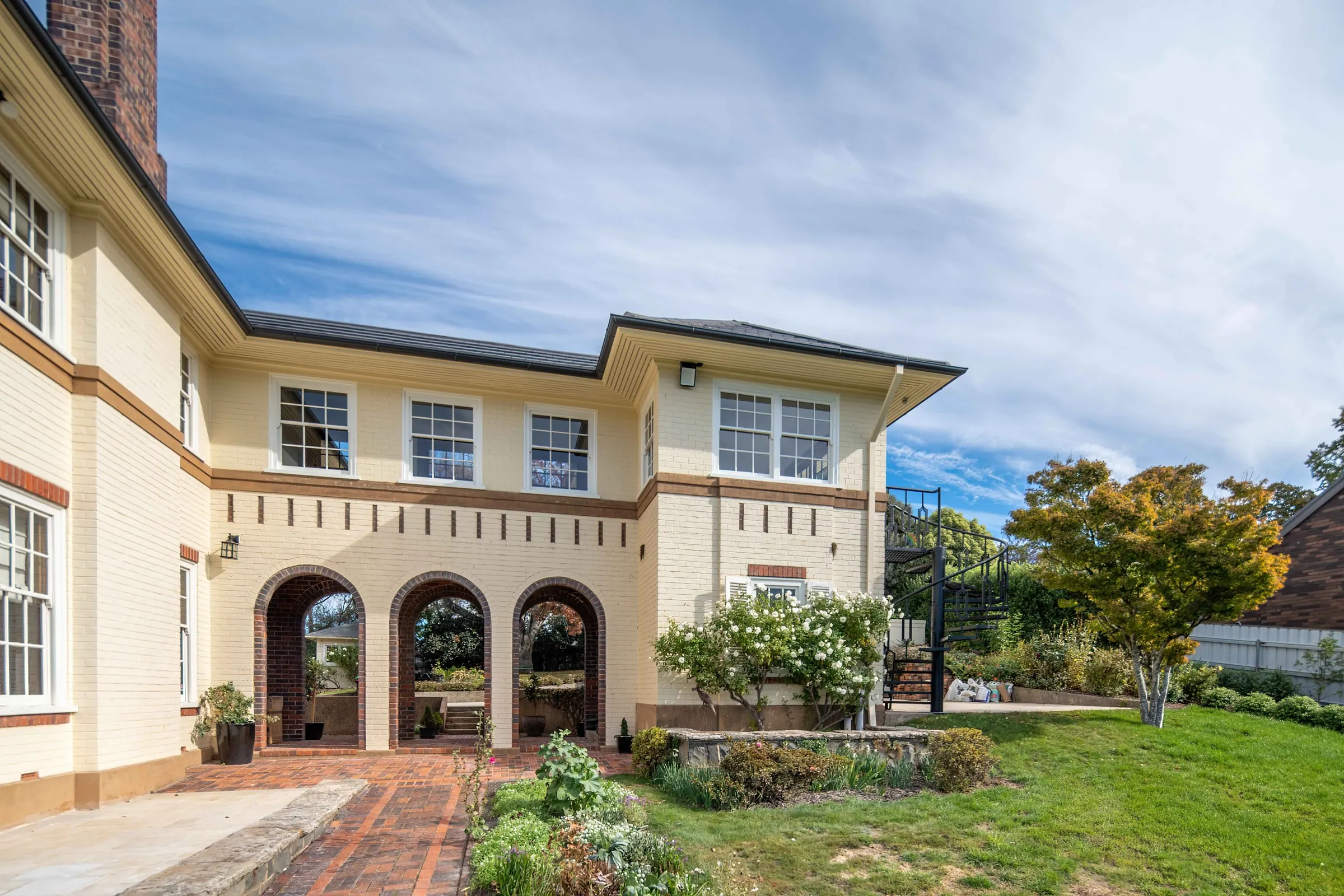 A finished rendered two-storey house with an arched carport, seen from the garden, East Launceston
