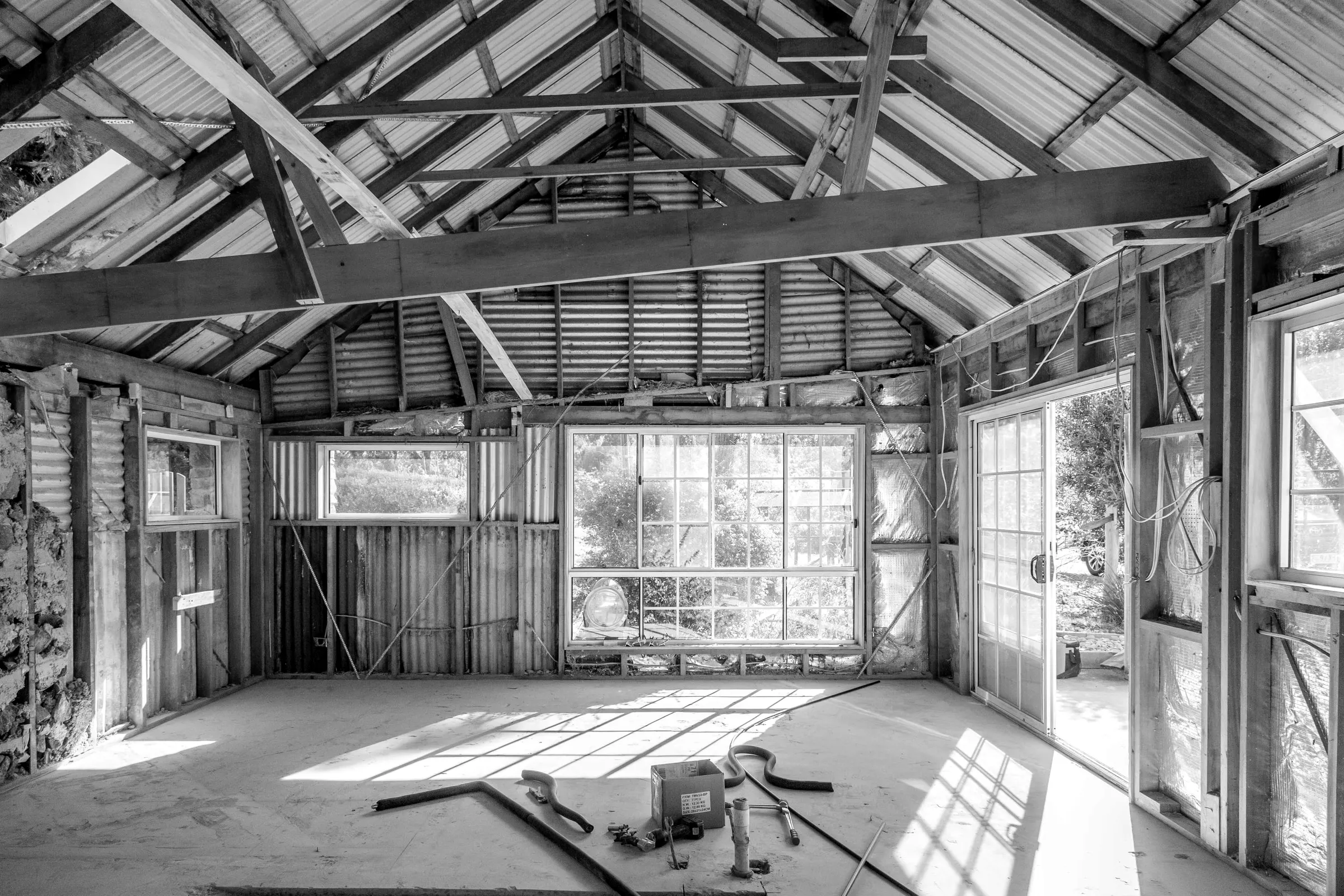 Roof framing and wall frames inside an old cottage being rebuilt, light coming through the end wall, Relbia