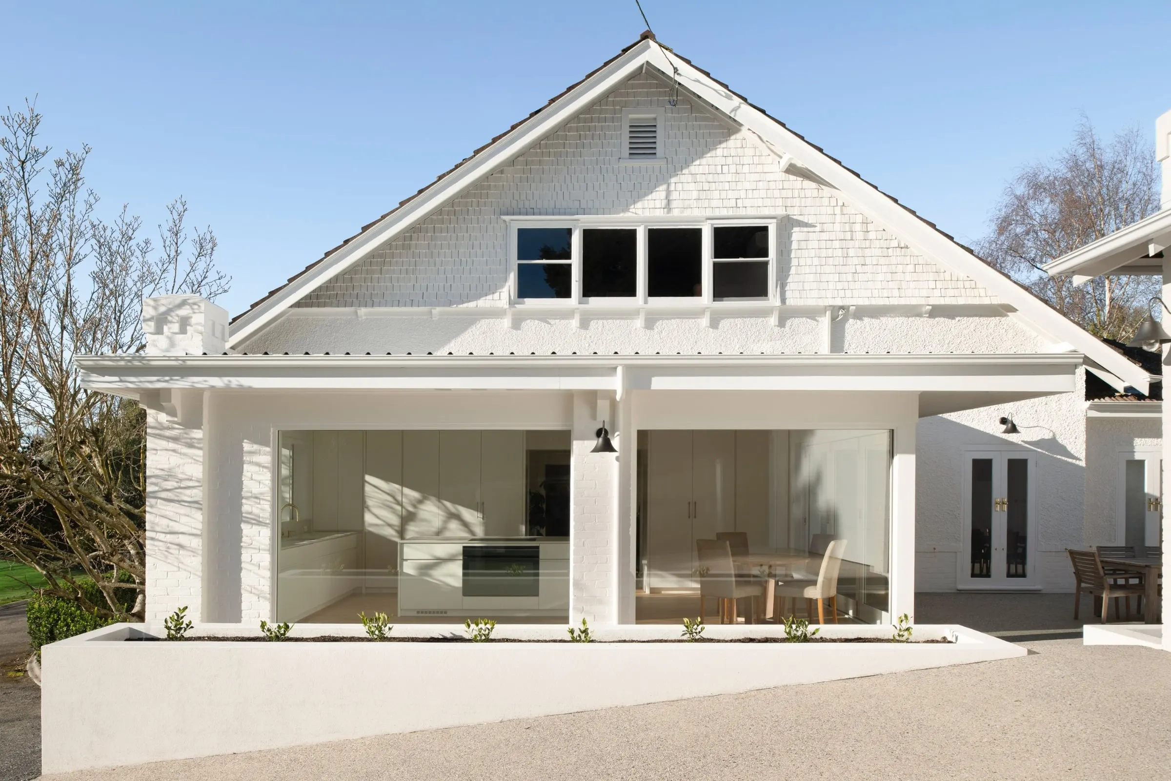 A finished white-painted house with a shingled gable and a deep covered verandah in afternoon light, Newstead
